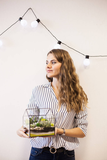 A girl holds a florariumov , glass shape with succulents, stones and sand, decorated with Christmas ribbons. Christmas gifts for home and office - 写真・画像