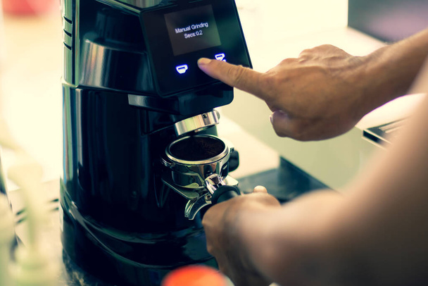 Prozess der Zubereitung von gebrühtem Kaffee in einem Kaffeehaus. Der Barista mahlt frisch geröstete Kaffeespezialitäten in eine professionelle Maschine. - Foto, Bild