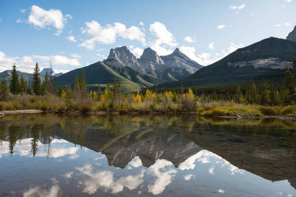 Scenery of Three Sisters Mountains reflection on Bow River in autumn forest at Canmore, AB, Canada - Фото, изображение