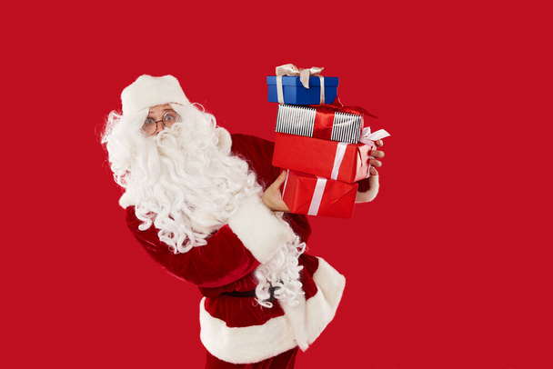 Happy Santa Claus holding boxes with gifts on a red background - Foto, afbeelding
