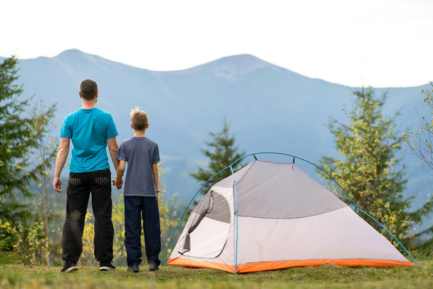 Az apa és a fia együtt sétálnak egy sátor mellett a nyári hegyekben. Aktív családi kikapcsolódás koncepciója. - Fotó, kép