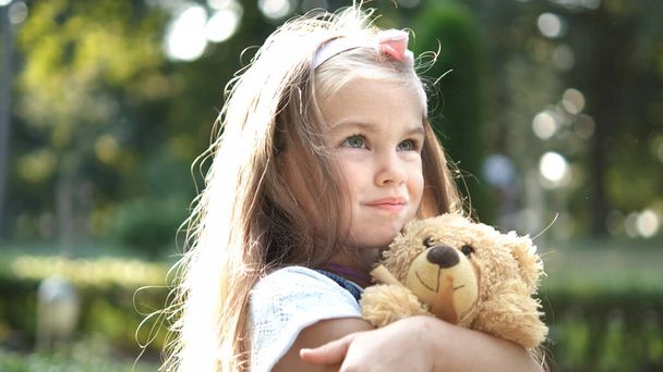 Pretty child girl playing with her favorite teddy bear toy outdoors in summer park. - Foto, immagini