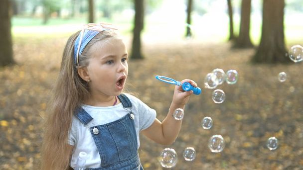緑の公園の外でシャボン玉を吹いている幸せな小さな子供の女の子。子供のコンセプトのための屋外夏の活動. - 写真・画像