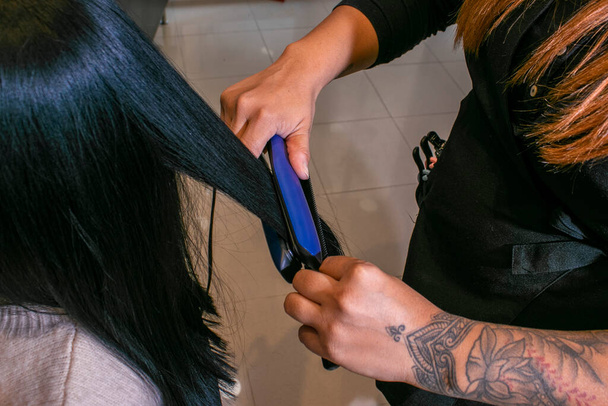 Parrucchiere utilizzando una piastra su una donna dai capelli neri - Foto, immagini