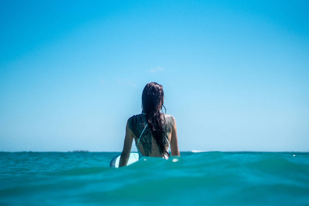 Portrait of surfer girl on surf board in blue ocean pictured from the water in Bali - Foto, Bild