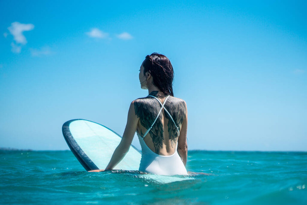 Portrait of surfer girl on surf board in blue ocean pictured from the water in Bali - Fotoğraf, Görsel