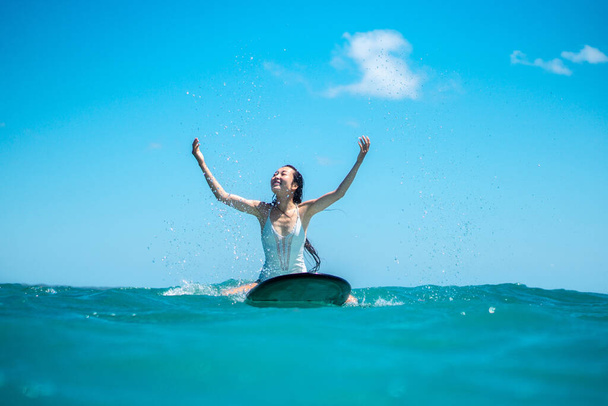 Portrait of surfer girl on surf board in blue ocean pictured from the water in Bali - Photo, Image