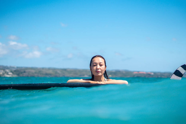 Portrait of surfer girl on surf board in blue ocean pictured from the water in Bali - 写真・画像