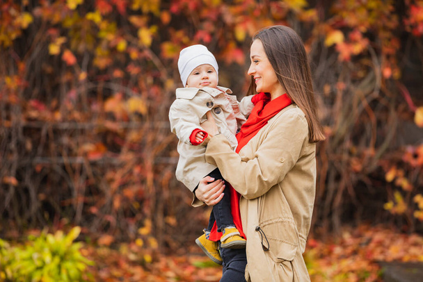 Η Μπέι με τη μαμά στο πάρκο. Μαμά και κόρη το φθινόπωρο. Η μαμά κρατάει το μωρό στην αγκαλιά της. Η μητέρα με την κορούλα της στο φθινοπωρινό πάρκο σε μια βόλτα. Πτώση Οικογένεια περπάτημα. - Φωτογραφία, εικόνα