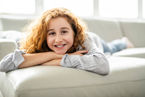 Positive redhead teenage girl lying on a couch. - Фото, изображение