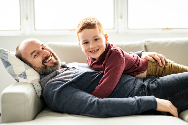 Father with redhead child having fun on the sofa at home - Valokuva, kuva