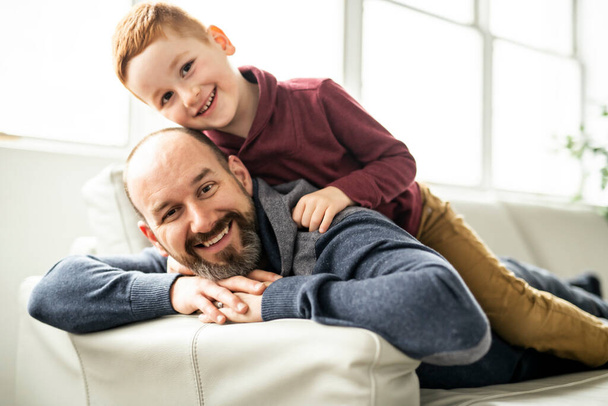 Father with redhead child having fun on the sofa at home - Φωτογραφία, εικόνα