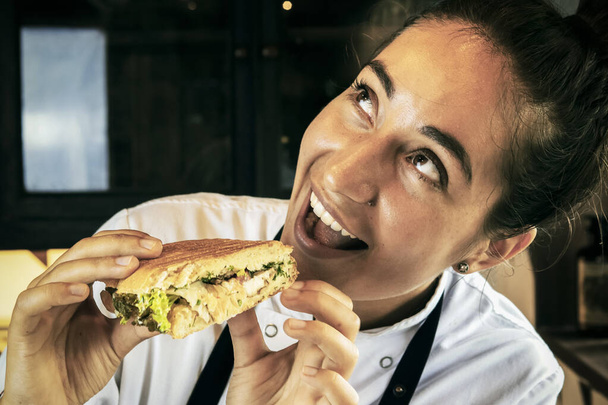 Happy woman chef eating sandwich. Close-up. Panini. Italian Cuisine. - Photo, image