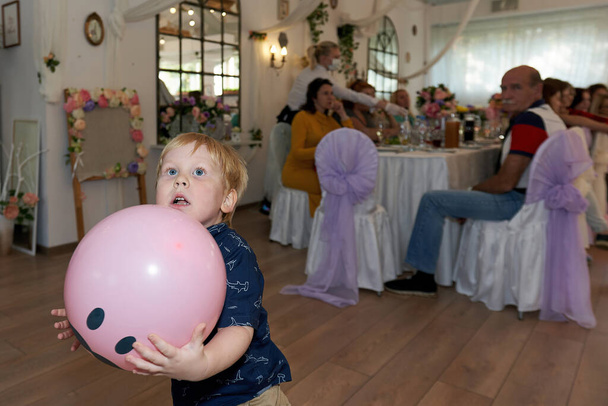Portrait of a child holding a large pink balloon in his hands in the banquet hall. Vertical shot, close-up - Foto, Imagem