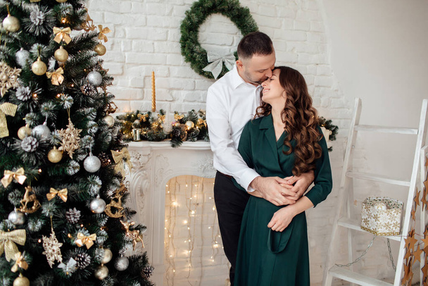 Celebrating Christmas together. Young couple in holiday clothes hugging near the Christmas tree. New Year, Valentine, love, romance concept - Foto, Imagem
