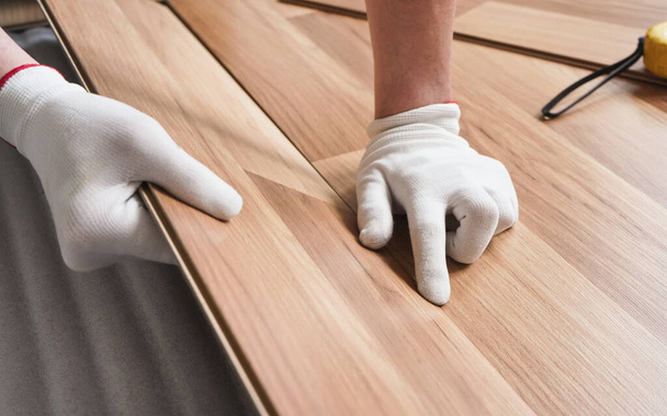 Installing laminated floor, detail on man hands in white gloves positioning wooden tile, over white foam base layer - Fotografie, Obrázek