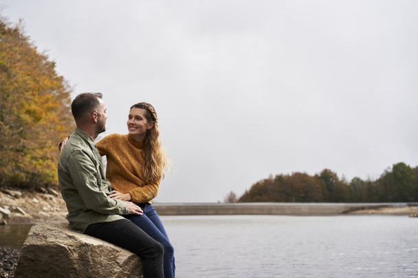 Para siedząca naprzeciwko jeziora i patrząca na siebie na zewnątrz z jeziorem w tle. - Zdjęcie, obraz