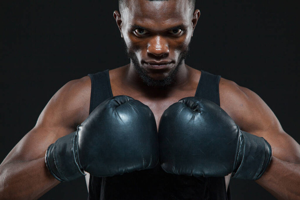 Front view shot of young African American boxer wearing gloves is posing isolated on a dark background - Photo, image