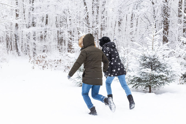 A young and beautiful couple is having fun in the snowy park, running and holding hands. Valentines Day concept. Winter season. - Valokuva, kuva