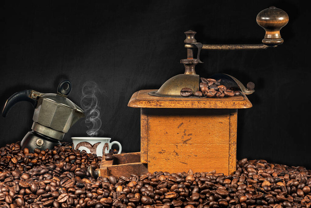 Old manual coffee grinder, Italian coffee maker and a cup on a pile of roasted coffee beans with empty blackboard in the background. - Photo, Image