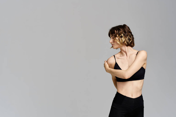 Una donna snella in leggings neri su uno sfondo grigio gesti con le mani ginnastica sport - Foto, immagini