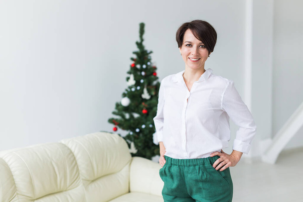 Счастливая молодая женщина в гостиной с рождественской елкой. Концепция праздников. - Фото, изображение