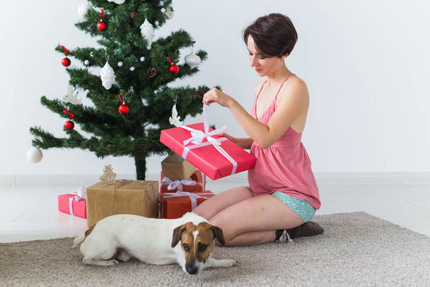 Noel ağacının altında hediye kutusunu açan sevimli köpeği olan mutlu genç bir kadın. Tatil kavramı. - Fotoğraf, Görsel