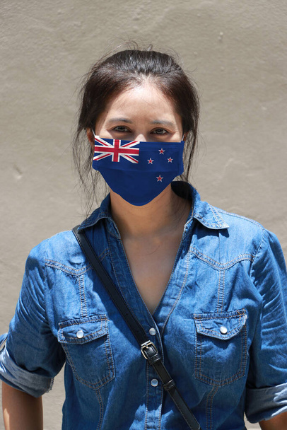 Bandera de Nueva Zelanda sobre máscara higiénica. Mujer enmascarada prevenir los gérmenes y usar vestido de mezclilla. Pequeña Protección de partículas o enfermedades respiratorias. Concepto de lucha contra la enfermedad. - Foto, imagen