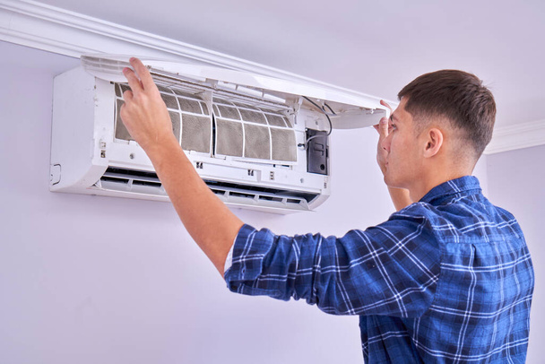 Caucasian male master in blue shirt cleans filters, installs and fixes air conditioner indoors - 写真・画像