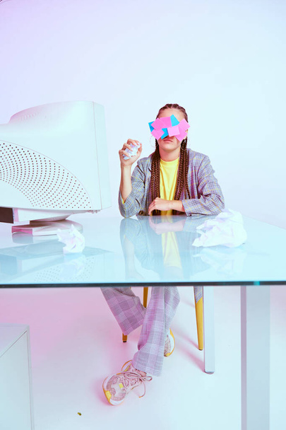 Κομψή γυναίκα υπάλληλος γραφείου με αυτοκόλλητα στο πρόσωπό της και τσαλακωμένο χαρτί κάθεται κοντά σε απαρχαιωμένο υπολογιστή - Φωτογραφία, εικόνα