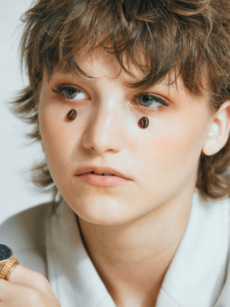 Coffee beans on young girl face like teardrops, stylish short haircut, female close up studio portrait - Φωτογραφία, εικόνα