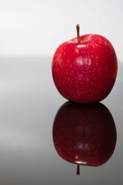 Свежее красное яблоко изолировано и отражено на поверхности черного стекла - Фото, изображение