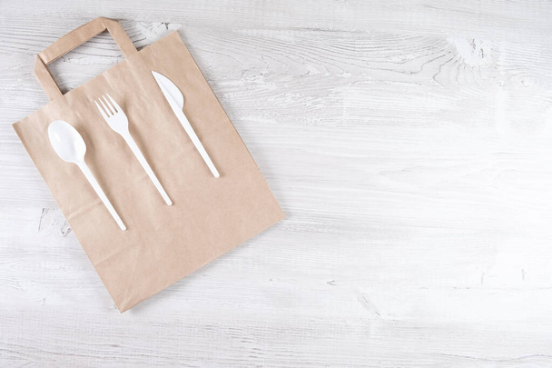 plastic fork, spoon, knife on paper bag. Eco-friendly food packaging and cotton eco bags on gray background with copy space. Carering of nature and recycling concept. containers for catering and - 写真・画像