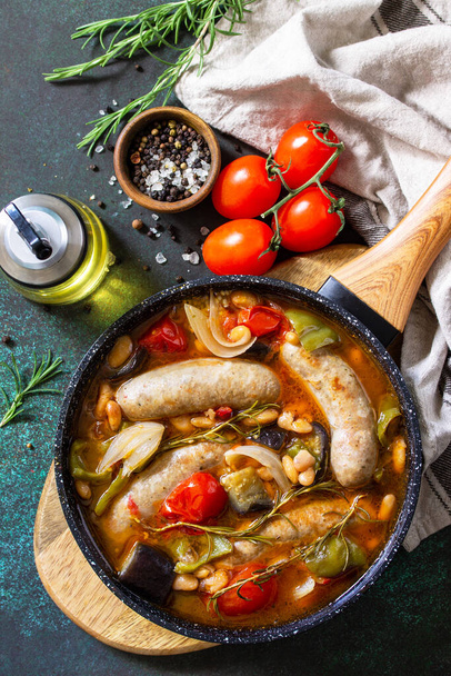 Stew smoked sausages with of beans, vegetables and tomato sauce in the pan on a stone countertop. Top view flat lay background. - Photo, Image