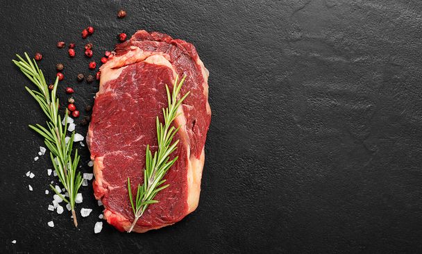 Сире м'ясо, яловичий стейк зі спеціями на чорному тлі, вид зверху
. - Фото, зображення
