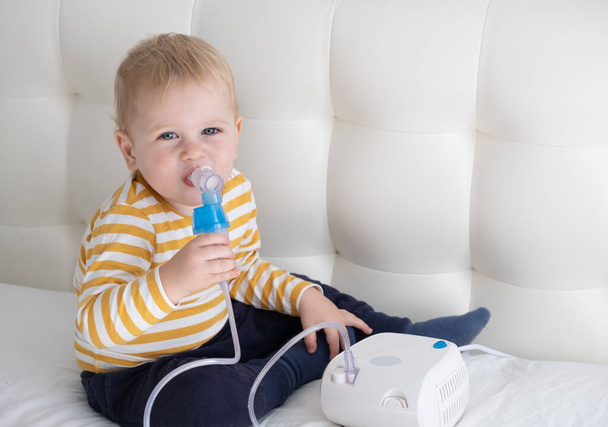 Little baby boy using steam inhaler nebulizer himself on the bed. copy space. health medical care. - Fotó, kép