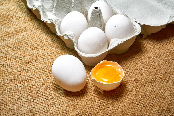 Свежие сырые куриные яйца в картонной коробке на фоне мешковины - Фото, изображение