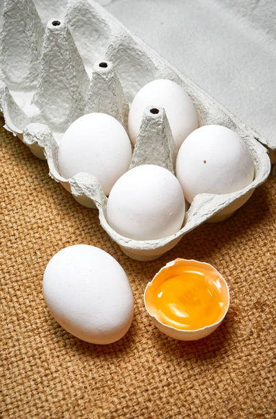 Свежие сырые куриные яйца в картонной коробке на фоне мешковины - Фото, изображение