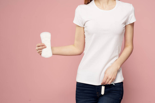 Woman with a tampon in her hand critical days hygiene white t-shirt jeans pink background menstrual cycle - Фото, изображение