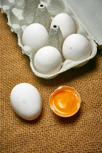 Świeże surowe jaja kurze w pudełku tekturowym na tle jutowym - Zdjęcie, obraz