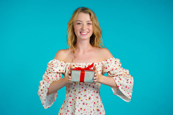 Excited woman holding gift box on blue wall background. Girl smiling, she is happy with present. Studio portrait - Photo, image