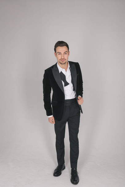 Studio portrait of a young caucasian man in a tuxedo, looking at the camera, standing against plain studio background - 写真・画像