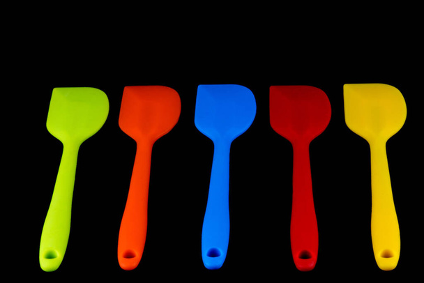 Coloured kitchen spatulas isolated against a black background - Photo, Image