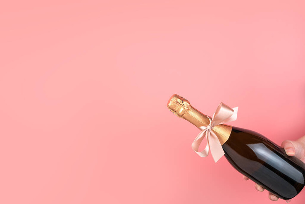 A bottle of champagne with a bow in hand on a pink background. - Photo, Image