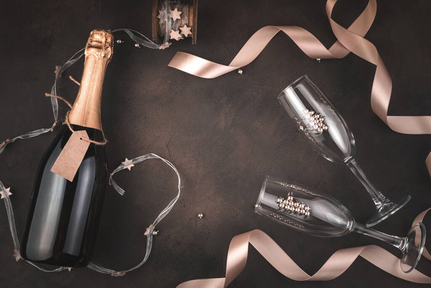 Fond de Noël stylisé avec une bouteille de champagne et des verres à vin sur fond brun. - Photo, image