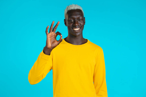 Mixed race man showing thumb up sign over blue background. Positive african guy smiles to camera. Winner. Success. Body language. - Фото, изображение