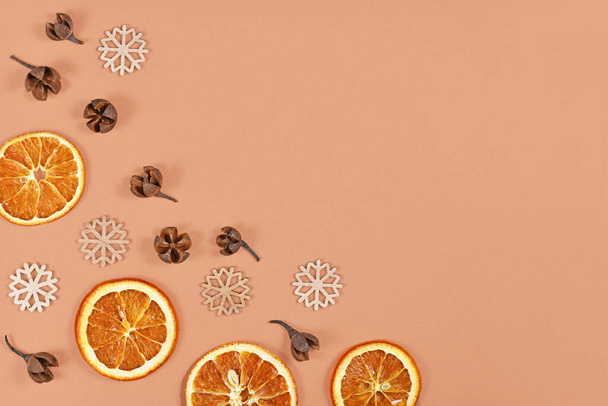 Seasonal winter flat lay with dried orange slices, fruit husks and wooden snowflake ornaments on cream colored background with empty copy space - Photo, image
