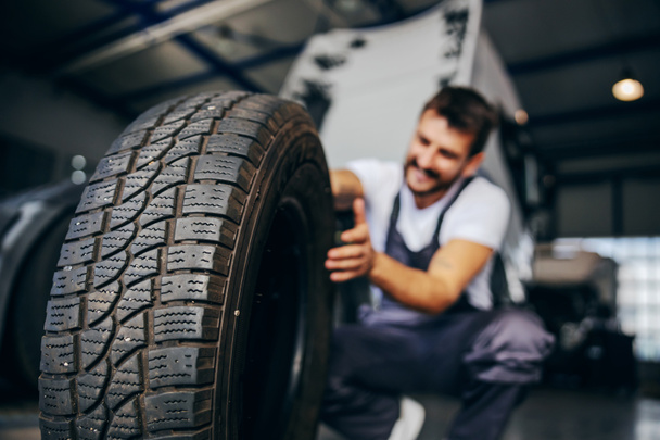 Hardworking experienced worker holding tire and he wants to change it. In background is truck. Selective focus on tire. - Photo, Image