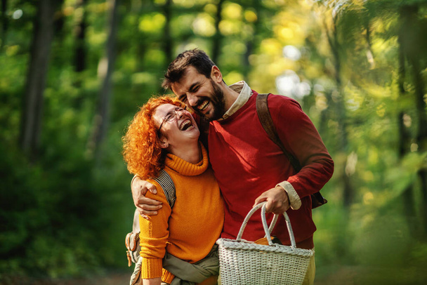 Joven feliz sonriente pareja enamorada abrazándose y caminando en la naturaleza. Pareja está sosteniendo equipo de picnic. Tiempo de otoño. - Foto, imagen