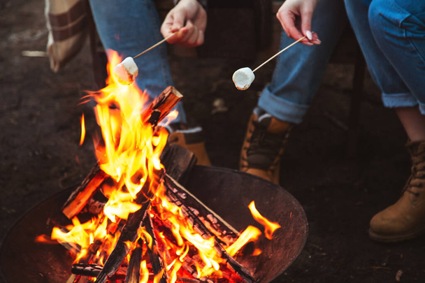 Loving couple prepares marshmallows by the fire. Autumn forest, romantic day. Selective focu - 写真・画像